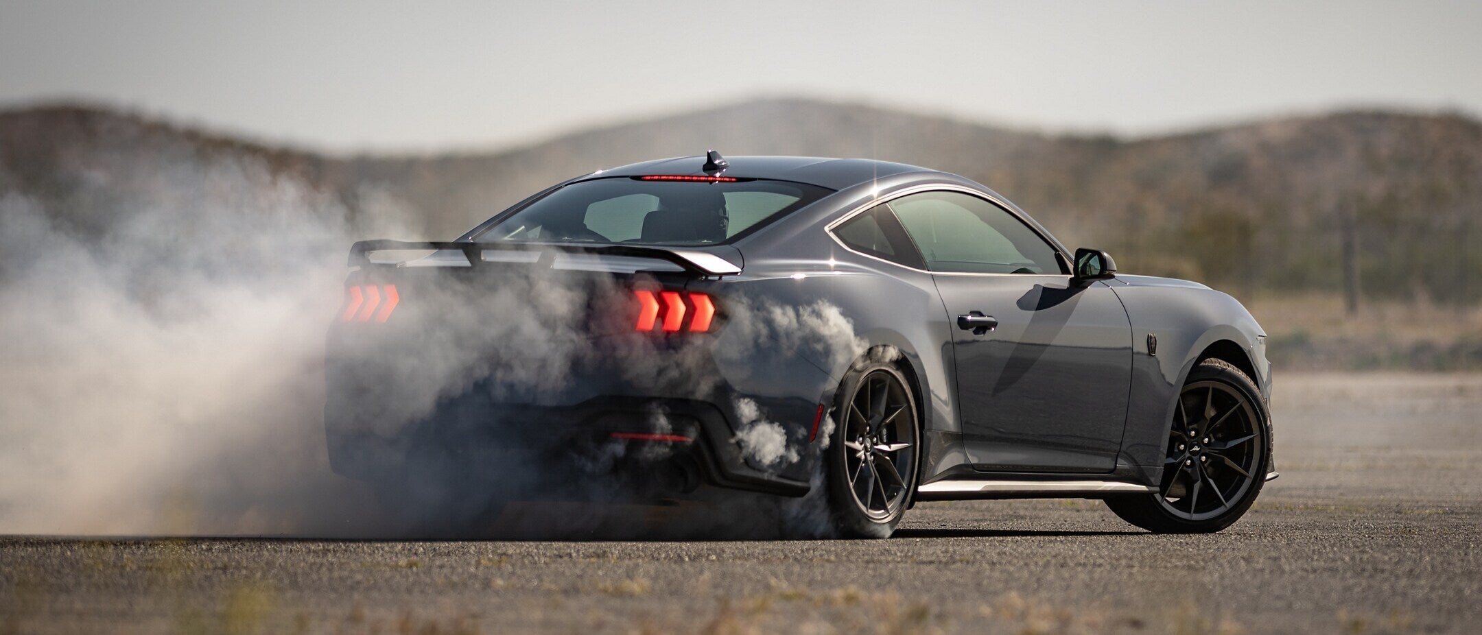 A gray mustang throwing up smoke.