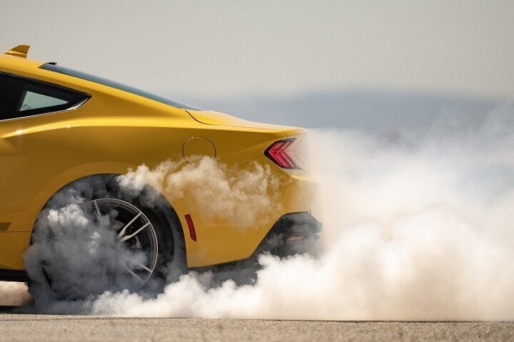A yellow mustang burning out.
