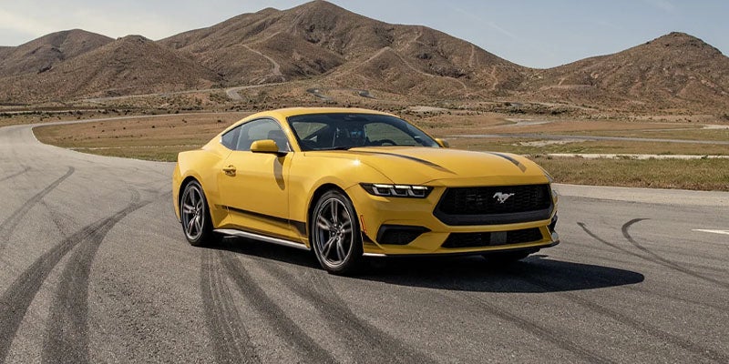 A yellow mustang sitting parked in the road.