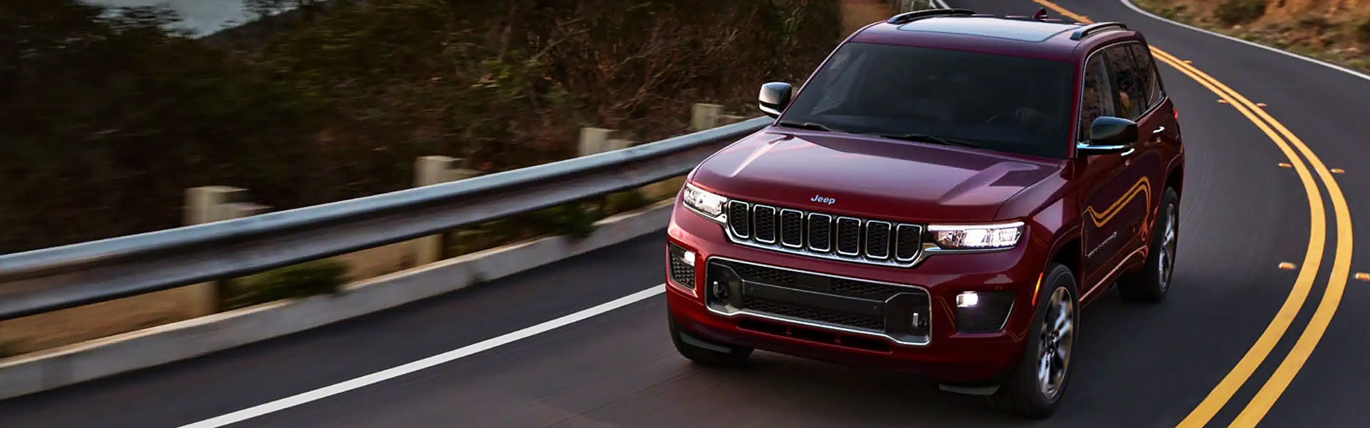 a jeep grand cherokee in red driving on a winding road at dusk