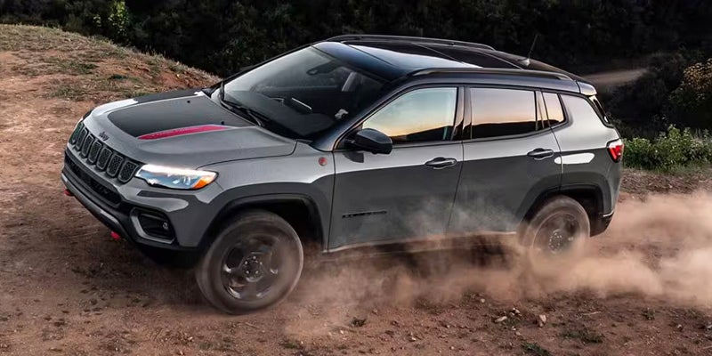 A gray jeep compass driving on a dirt road.