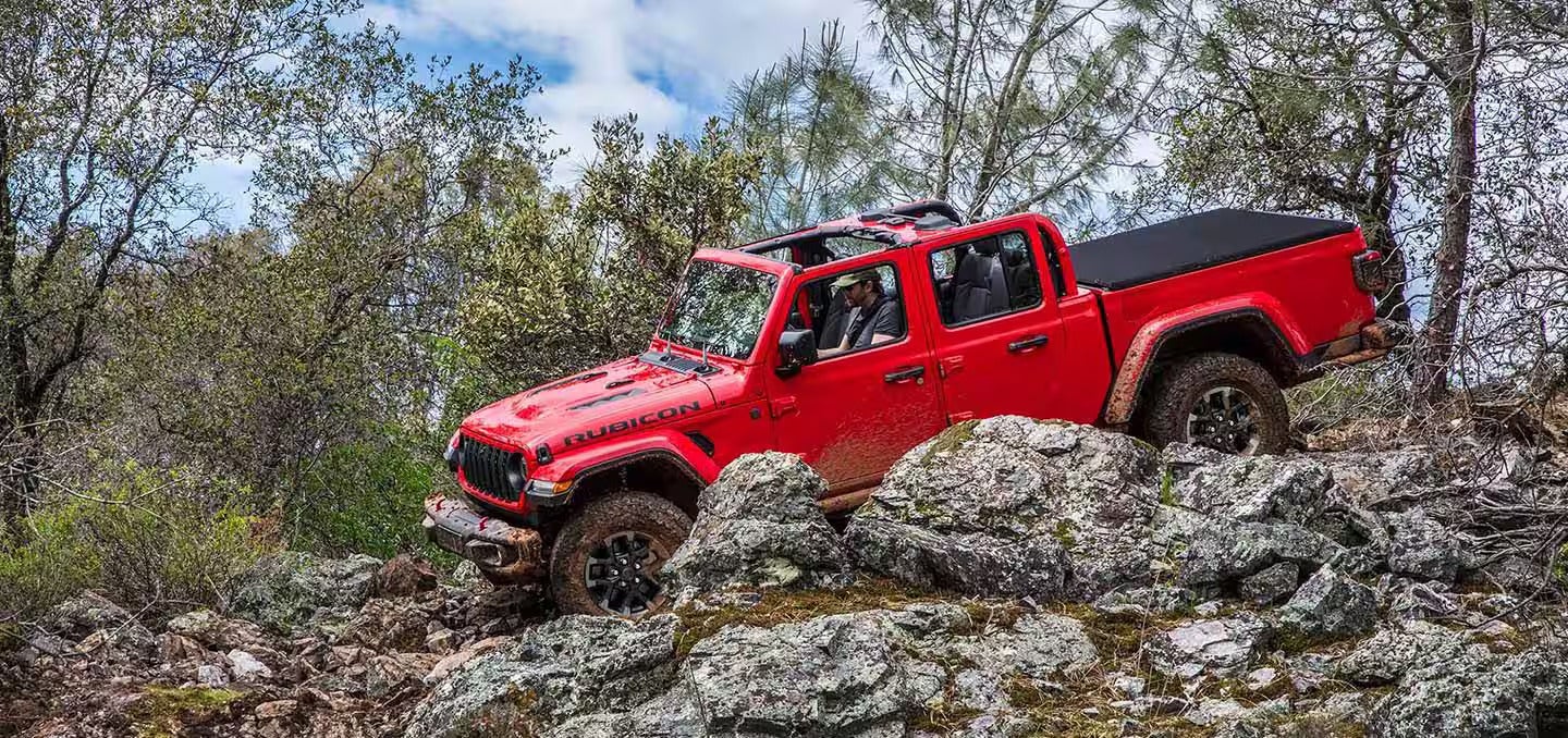 A red jeep driving down some rocks.