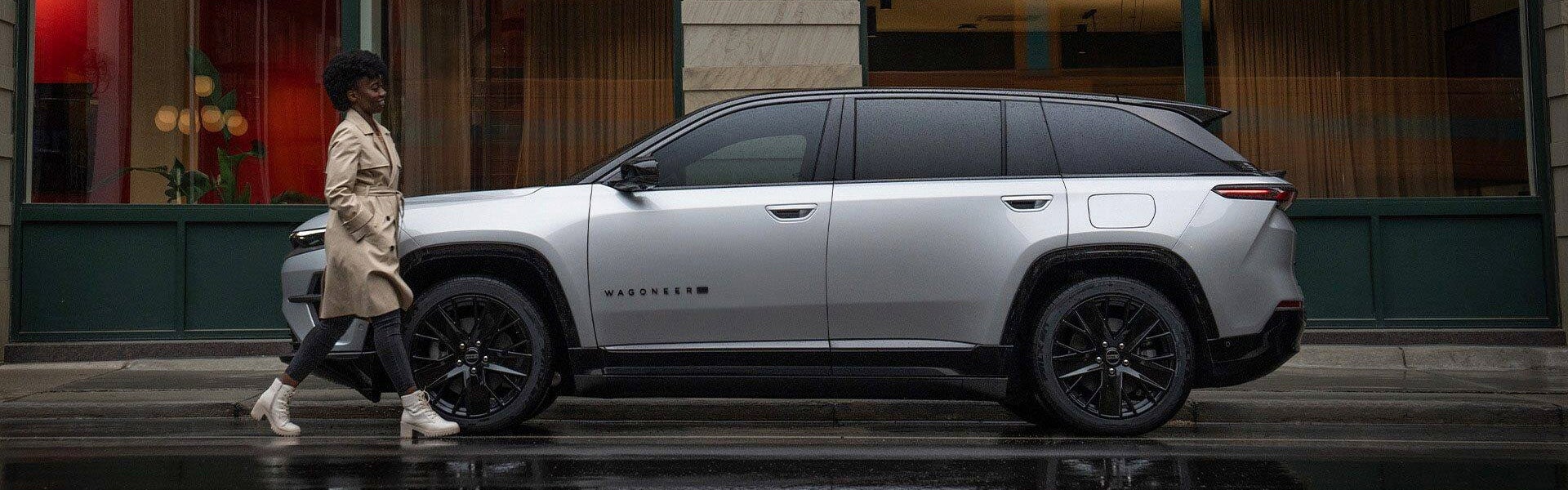 A woman walking next to a silver wagoneer s.