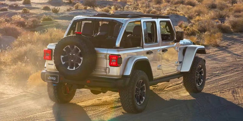 A silver jeep driving on a dirt road.