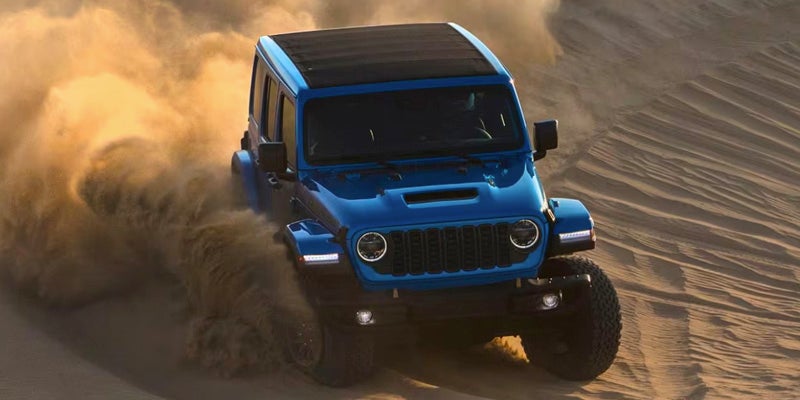 A blue jeep driving through the sand.