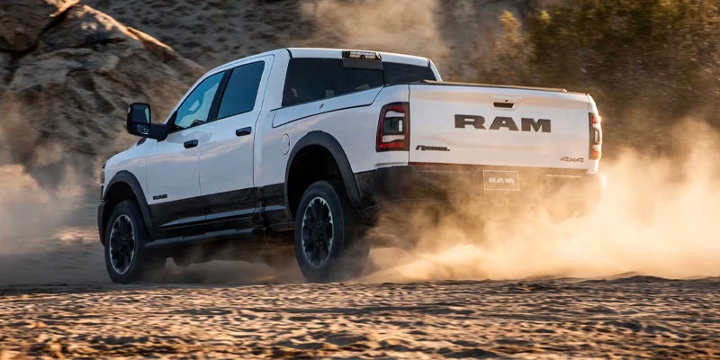 A white ram truck driving on a dirt road.