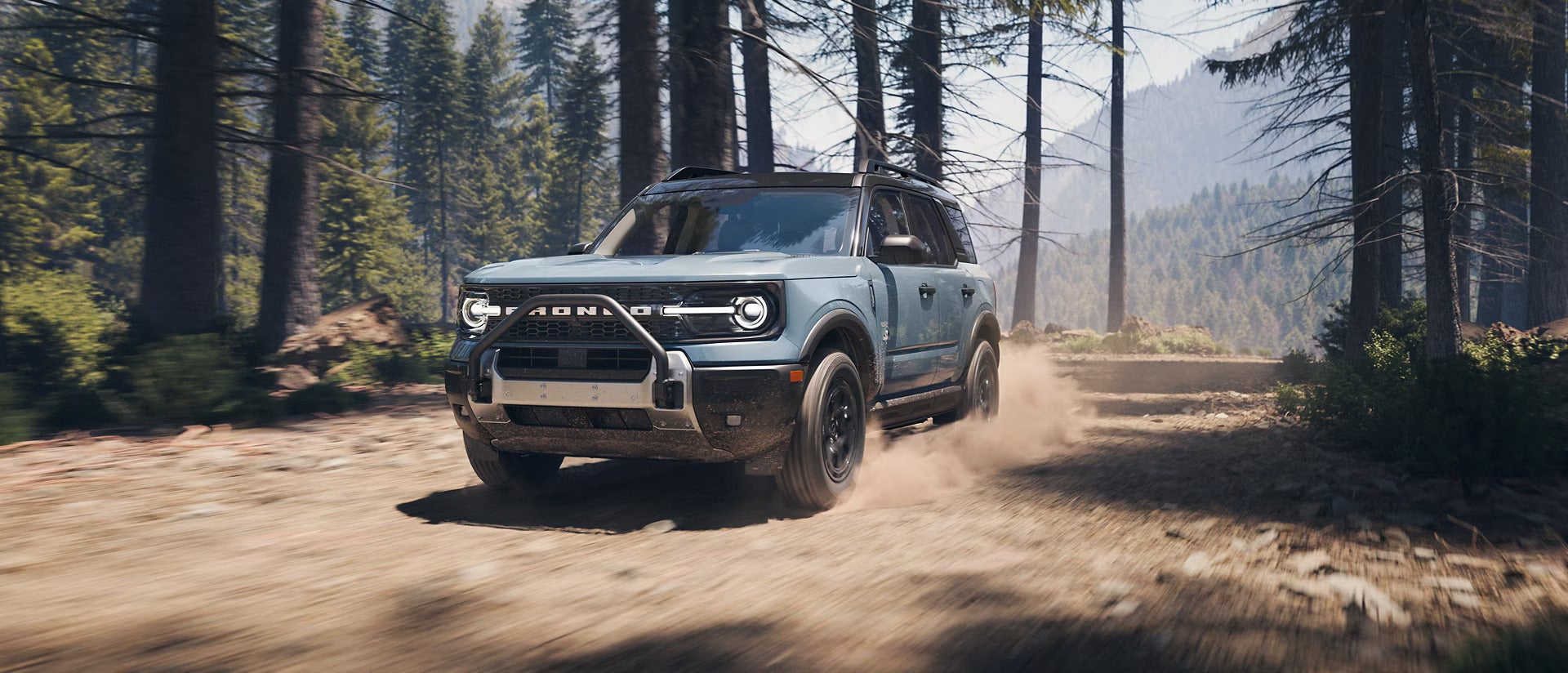A blue bronco driving through the woods.