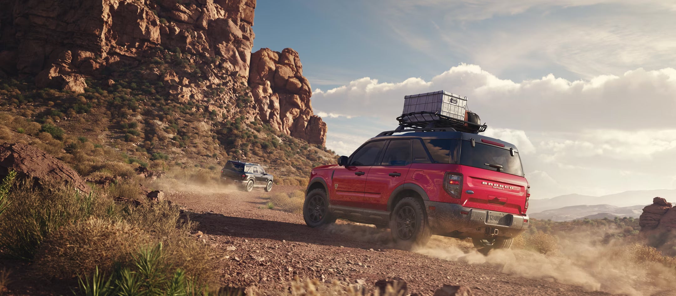 A red bronco sport driving on a dirt road.