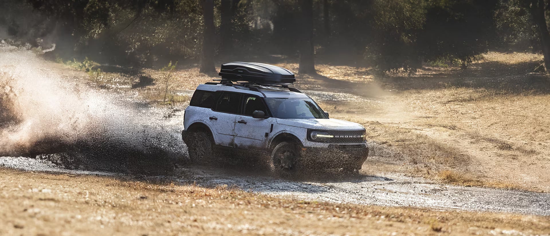 A white bronco sport driving through the mud.
