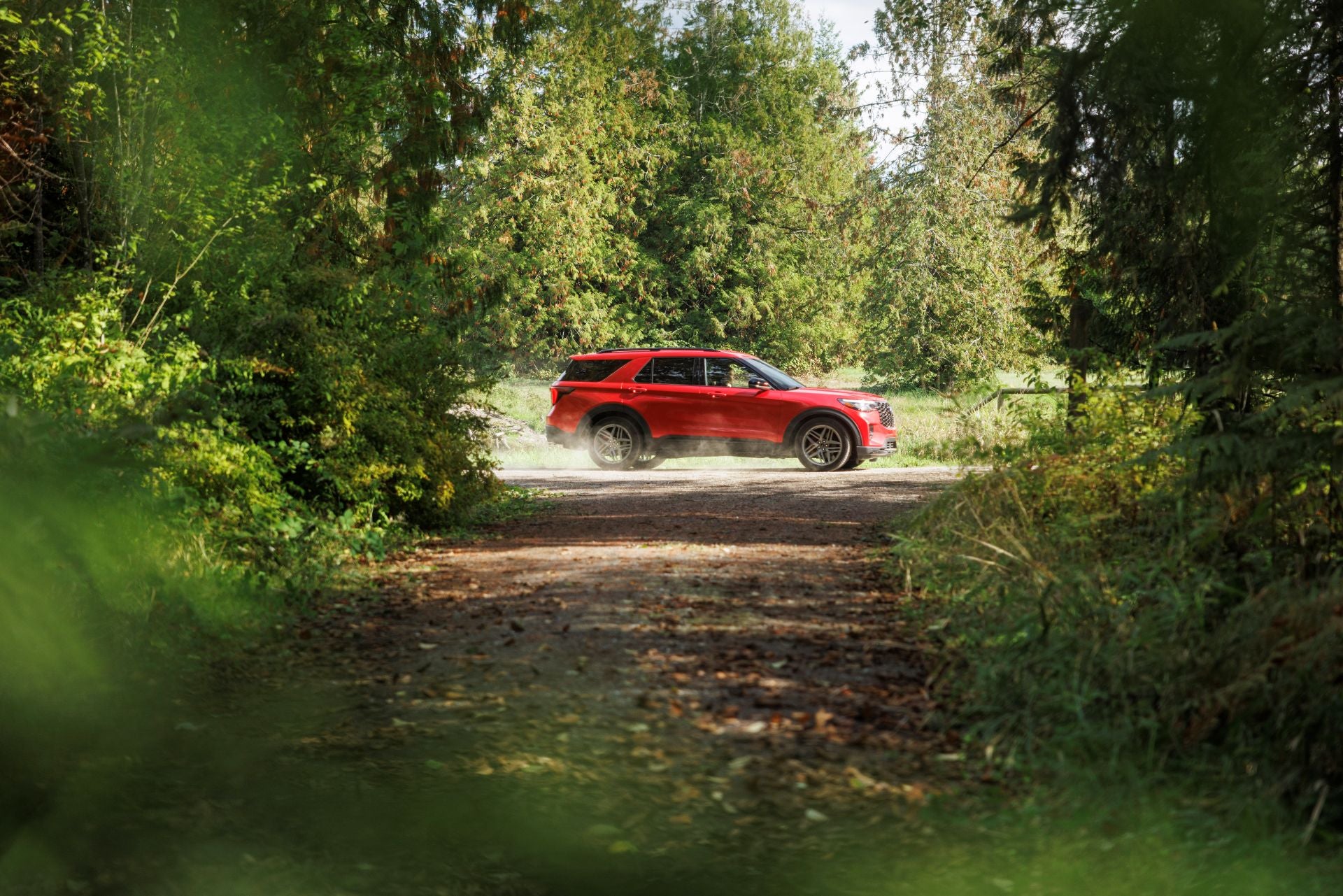 A red suv driving through the woods.