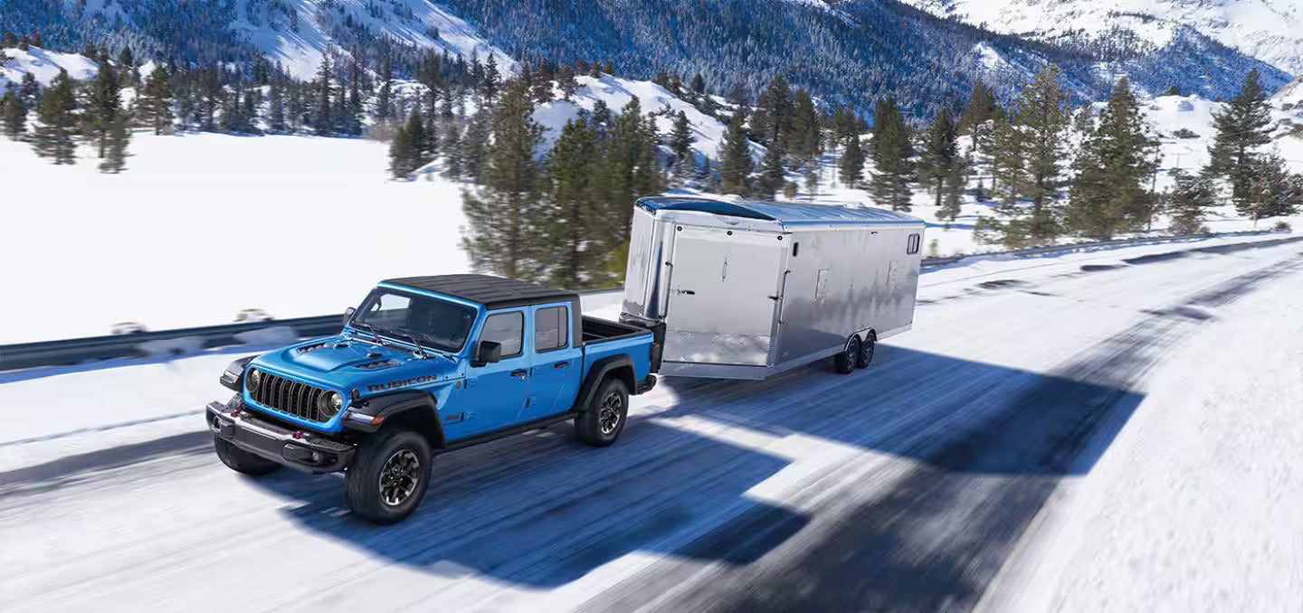 A blue jeep pulling a trailer in the snow.
