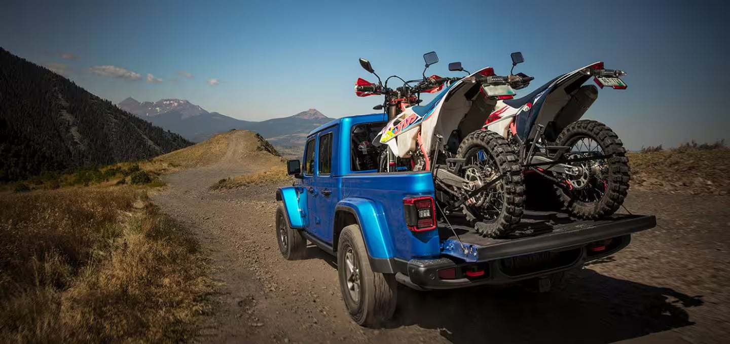 A blue jeep with two dirt bikes in the back.