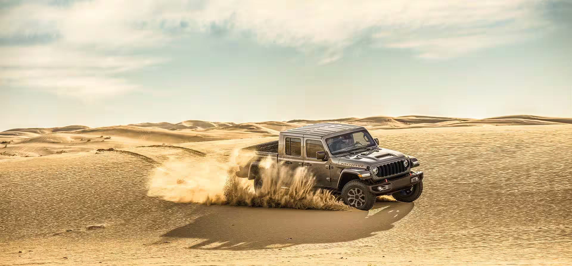 A silver jeep driving through the sand.