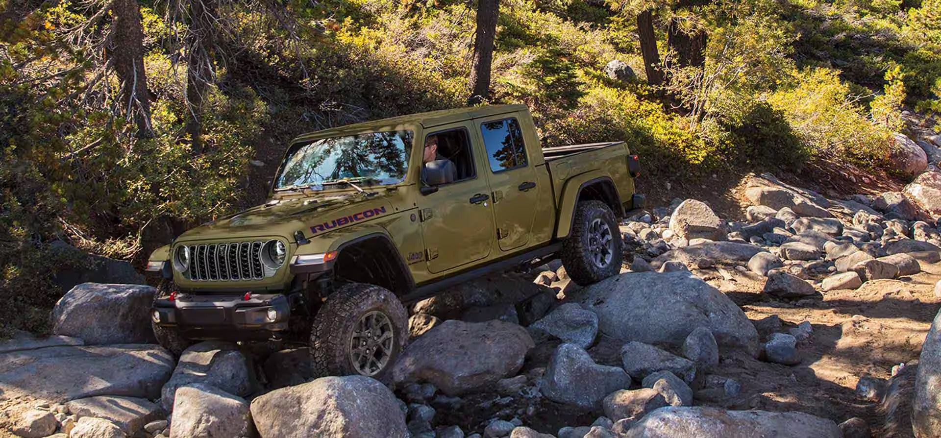 A green jeep driving over some rocks.