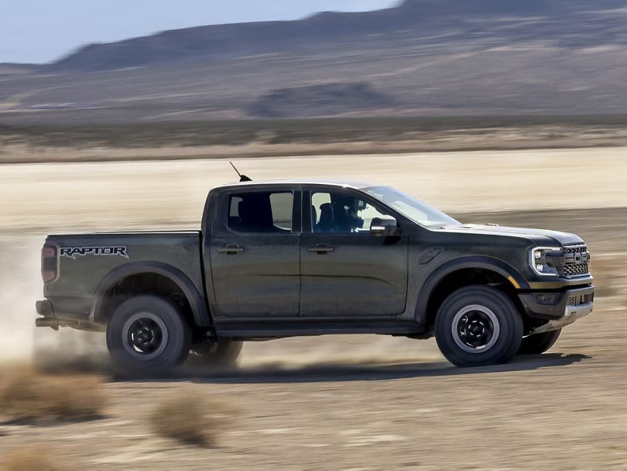 A green truck driving on a dirt path.