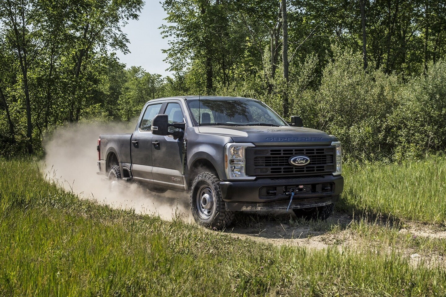 A blue truck driving on a dusty trail.