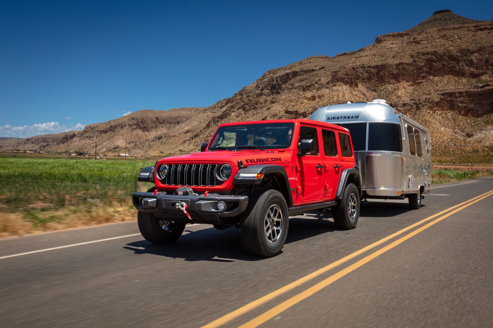 A red jeep wrangler pulling a trailer down the road.