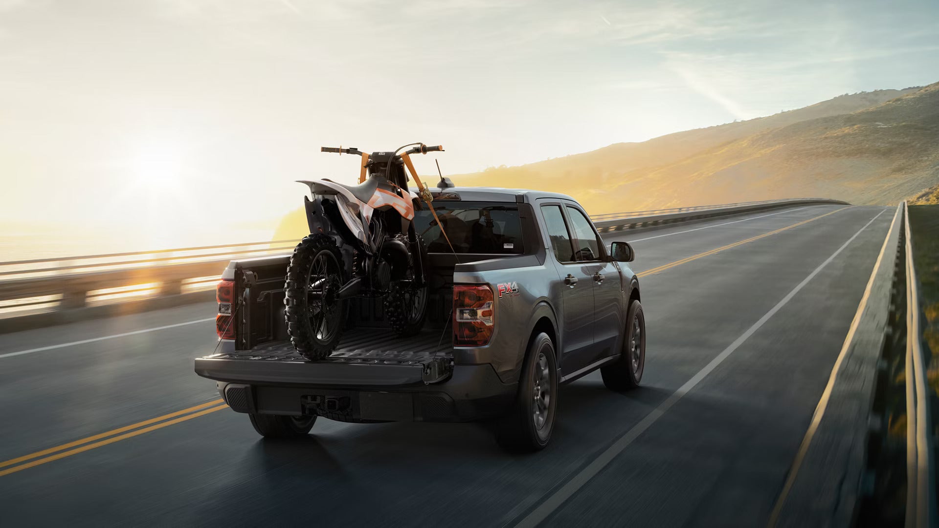 A New 2026 Ford Maverick driving down a road hauling a dirt bike