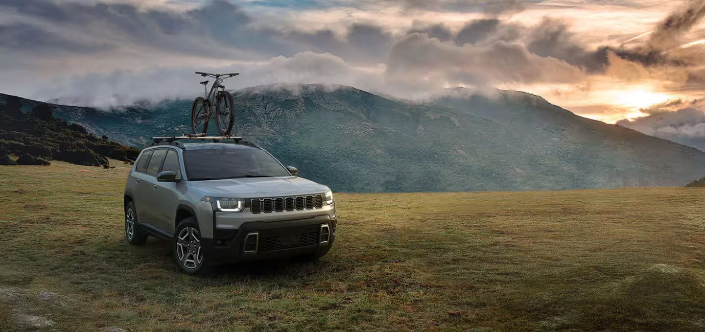 2026 Jeep Cherokee parked in the grass with a mountain in the back ground