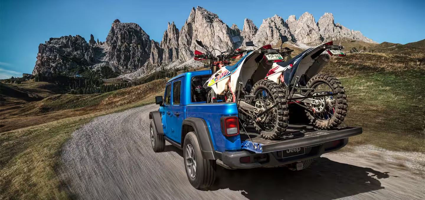 2026 Jeep Gladiator parked on a hill with two dirt bikes in the bed of the gladiator