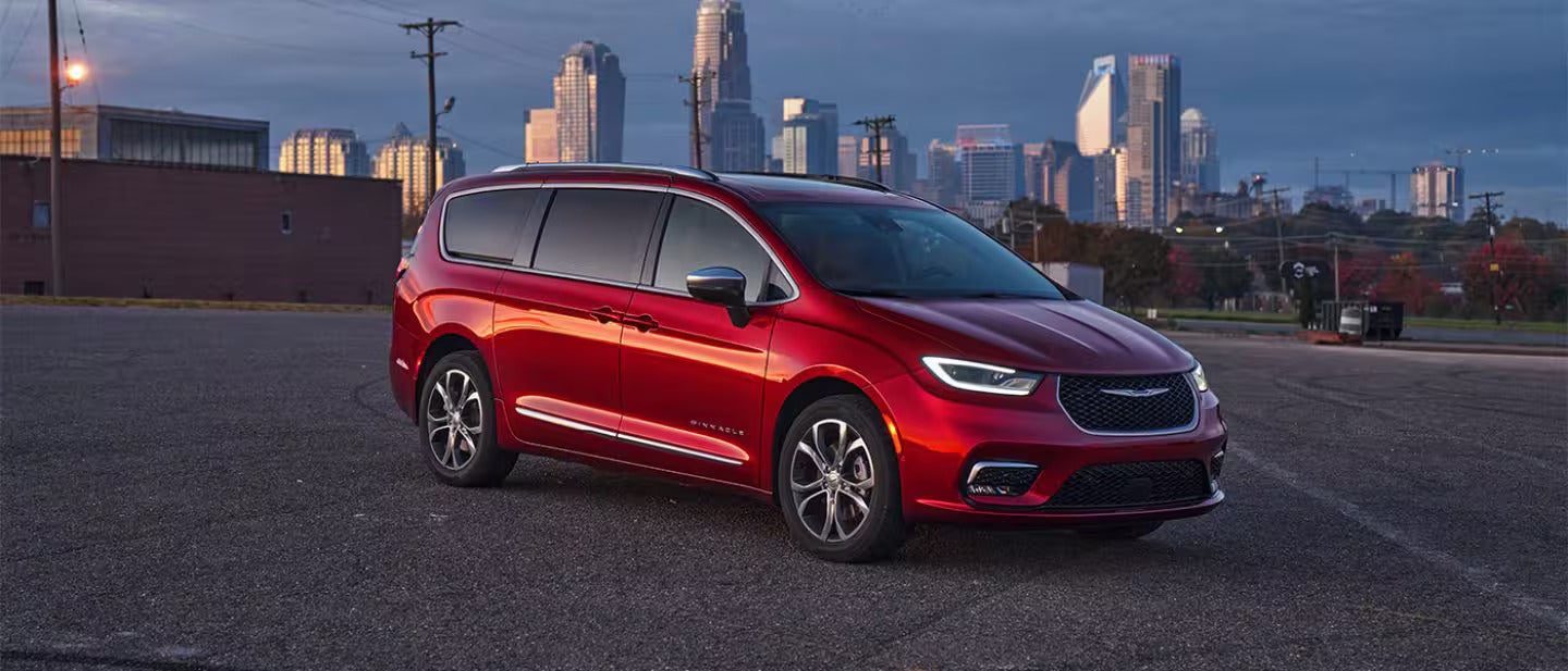 A red 2026 Chrysler Pacifica parked on a road with the city in the back ground