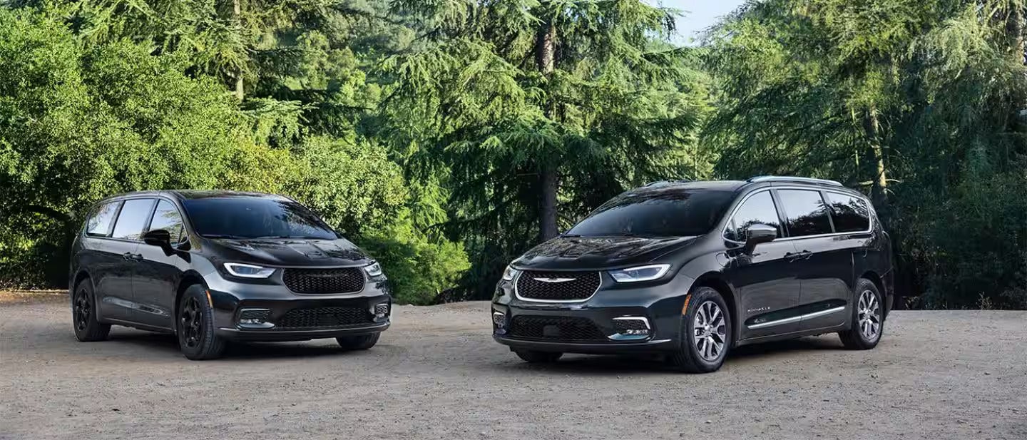 two black 2026 pacifica plug-in hybrid's parked on a road with trees in the back ground