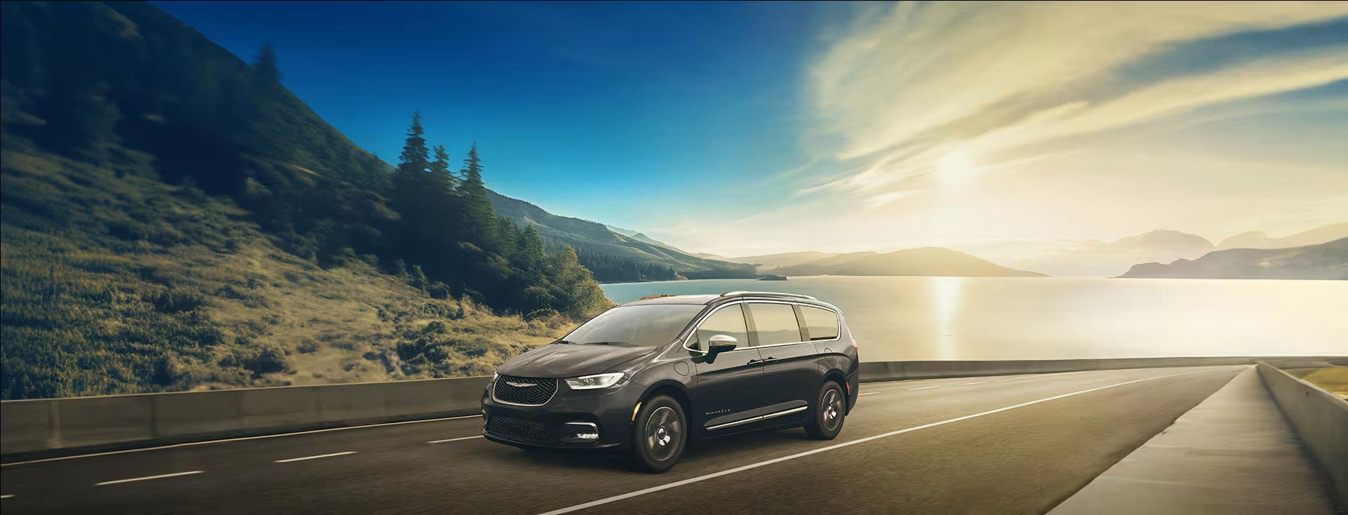 two black 2026 pacifica plug-in hybrid's parked on a road with trees in the back ground