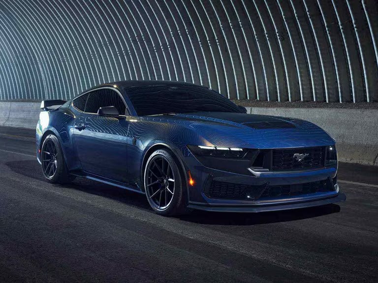 a dark blue ford mustang dark horse driving on a track at night
